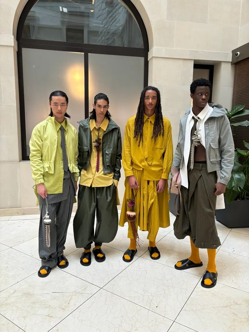 Four models standing together in a stone courtyard in mustard, lime, olive and grey clothing