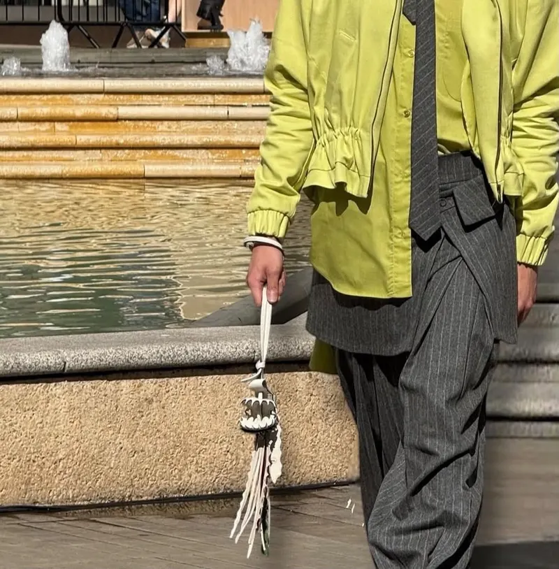 Detail of a lime-green jacket worn over pinstripe trousers, holding a tasselled accessory