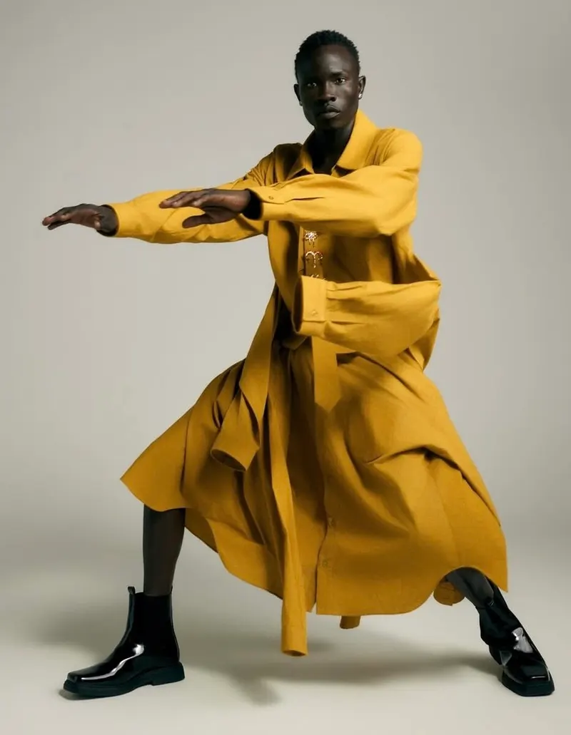 Studio portrait of a model in an ochre coat and black boots, arms extended